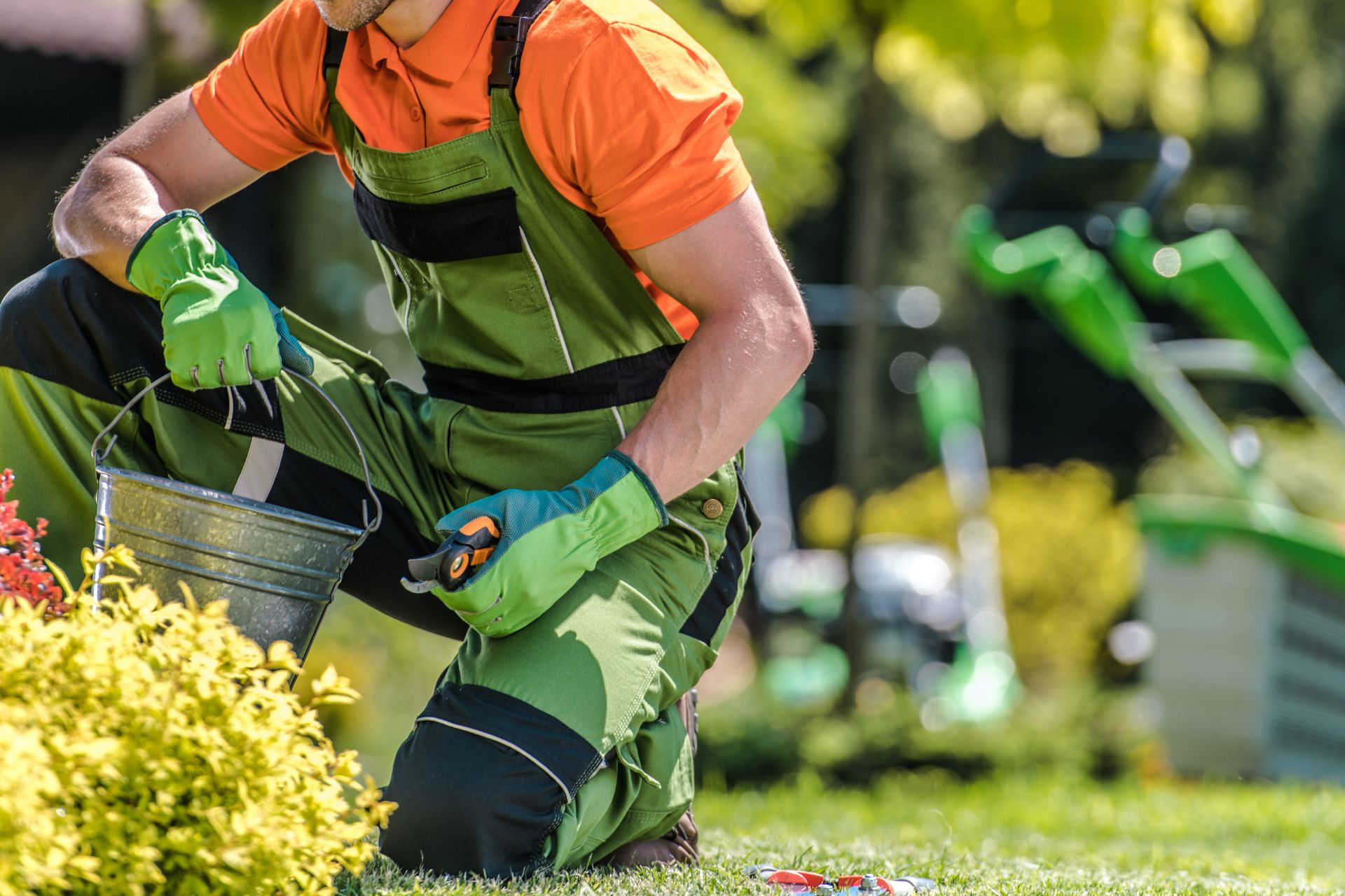Jardinier en tenue de travail verte et orange effectuant l'entretien d'un espace vert avec outils professionnels