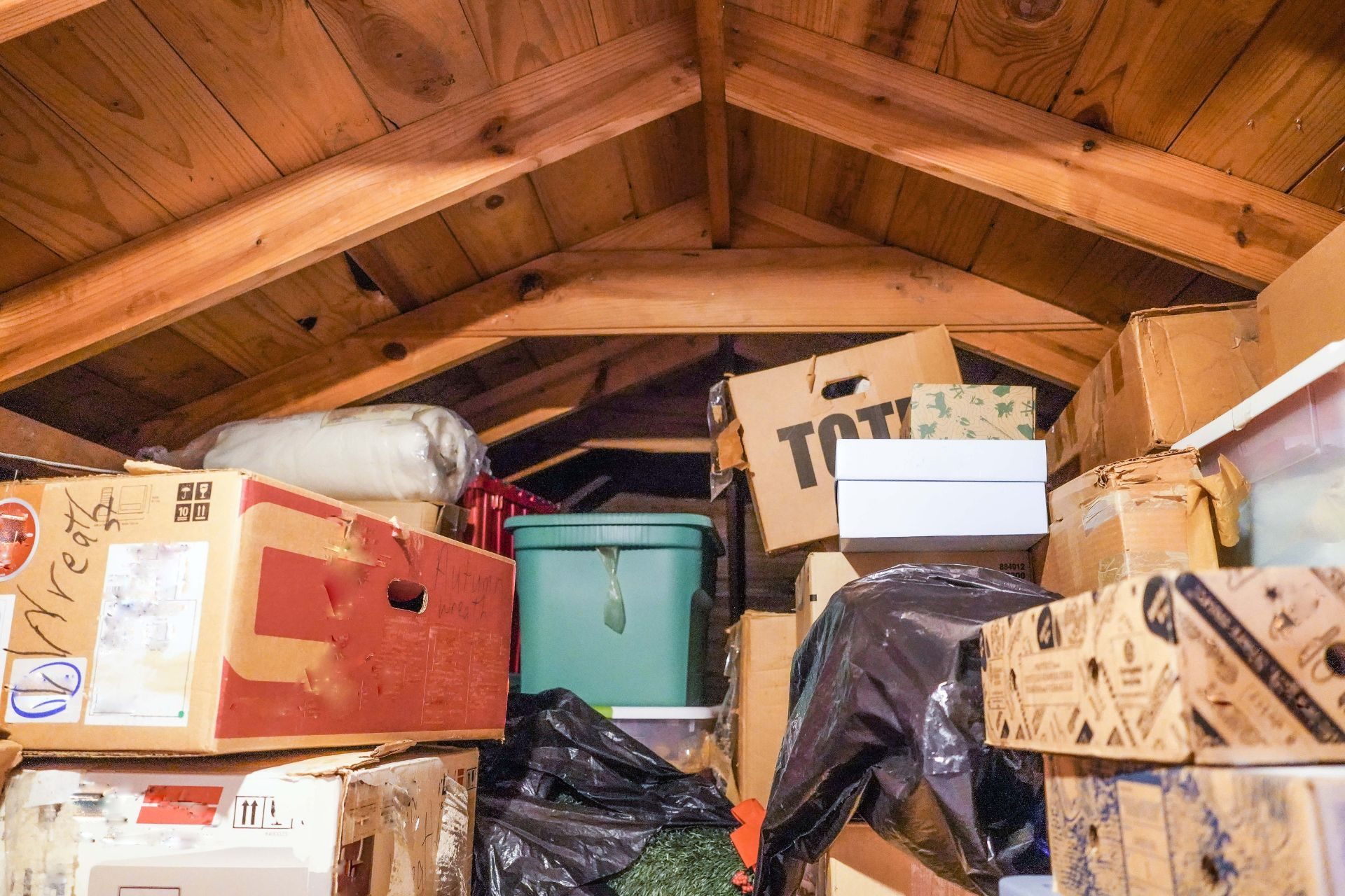 Grenier encombré avec cartons, boîtes en carton, container turquoise, sacs noirs et charpente bois apparente