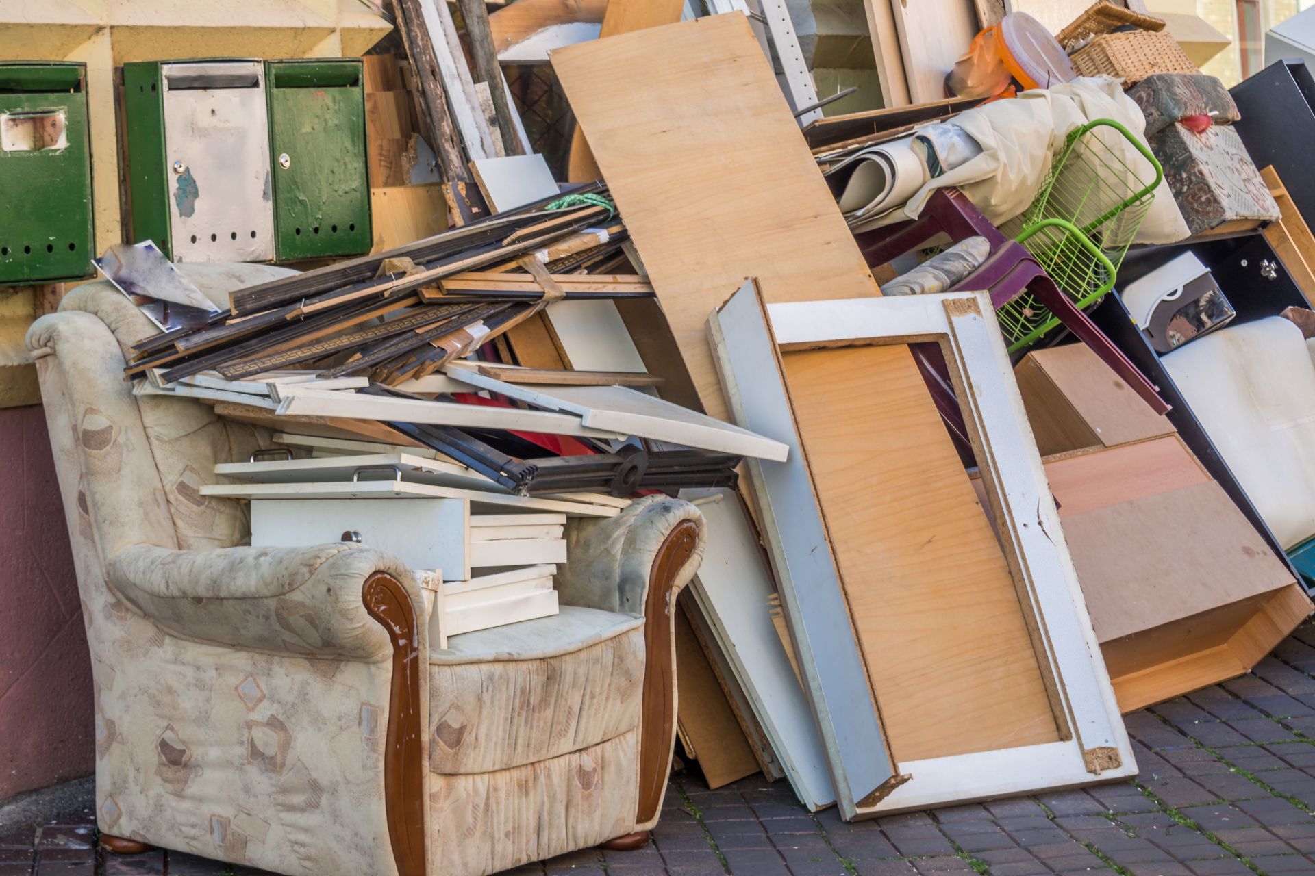 Accumulation d'encombrants et de meubles usagés empilés dans un espace de débarras, incluant fauteuil beige, portes vertes
